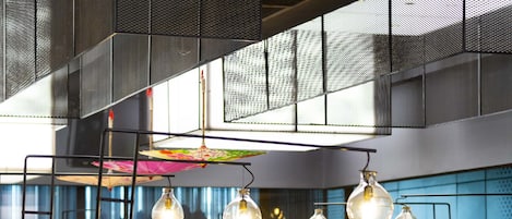 Et moderne restaurantinteriør med høje lofter, hængende lamper og forskellige sidearrangementer, herunder båse og borde.