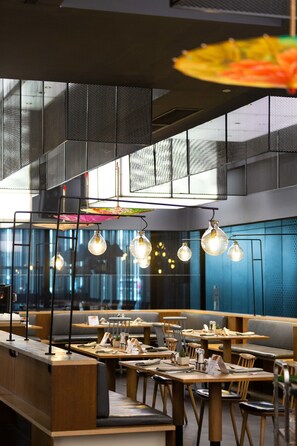 A modern restaurant interior with high ceilings, hanging light fixtures, and a mix of seating arrangements including booths and tables. - Le Méridien Zhengzhou (Zhengzhou)