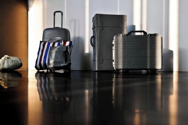 Una habitación con piso reflectante, una maleta, una bolsa de deporte y una maleta grande gris.
