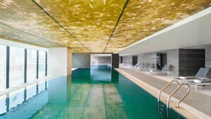 Una piscina interior con agua cristalina, techo iluminado por el sol y sillones de descanso a lo largo del borde.