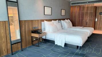 A hotel room with two beds, a bedside table with a phone, a mirror, and framed artwork on the wall.