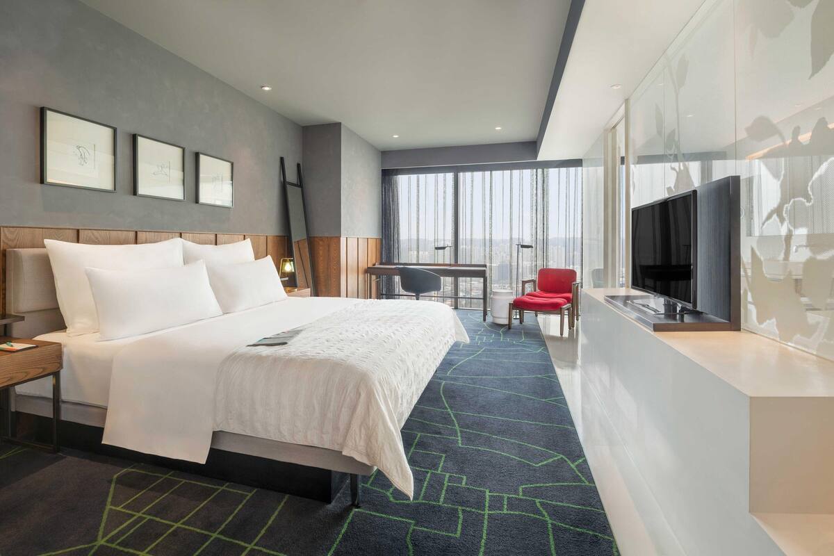 Een moderne hotelkamer met een groot bed, een bureau met stoel, een televisie en een balkon met uitzicht op de stad.