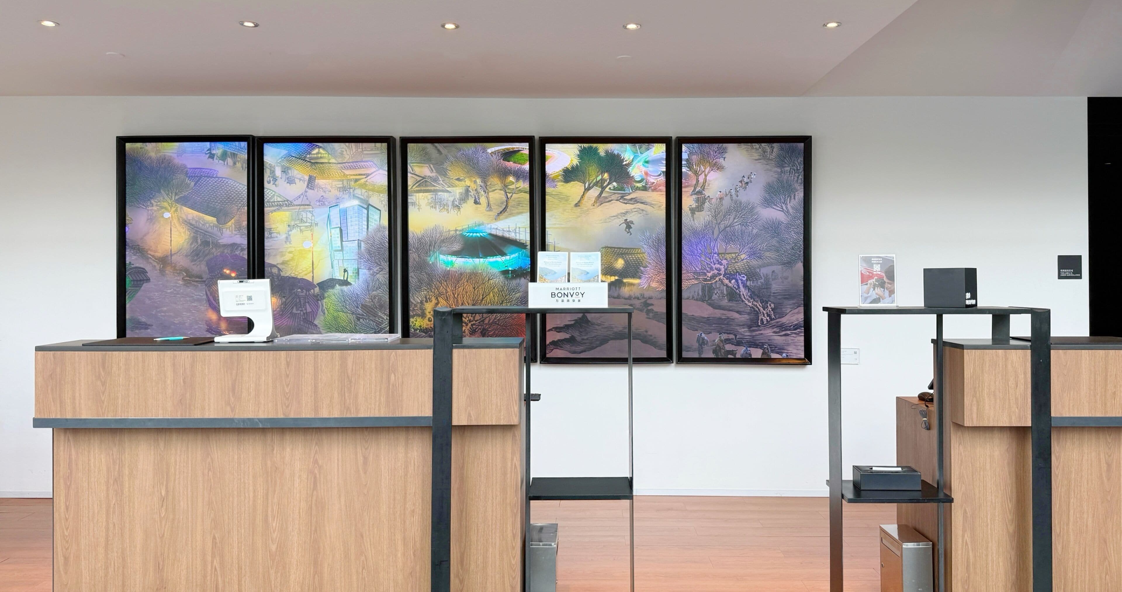 Un mostrador de recepción con pantalla digital, cuadros en la pared y un cartel que indica un hotel Marriott Bonvoy.
