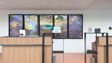 Un mostrador de recepción con pantalla digital, cuadros en la pared y un cartel que indica un hotel Marriott Bonvoy.