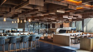 Un bar moderno con una barra central, taburetes y una zona de estar con mesas y sillas.