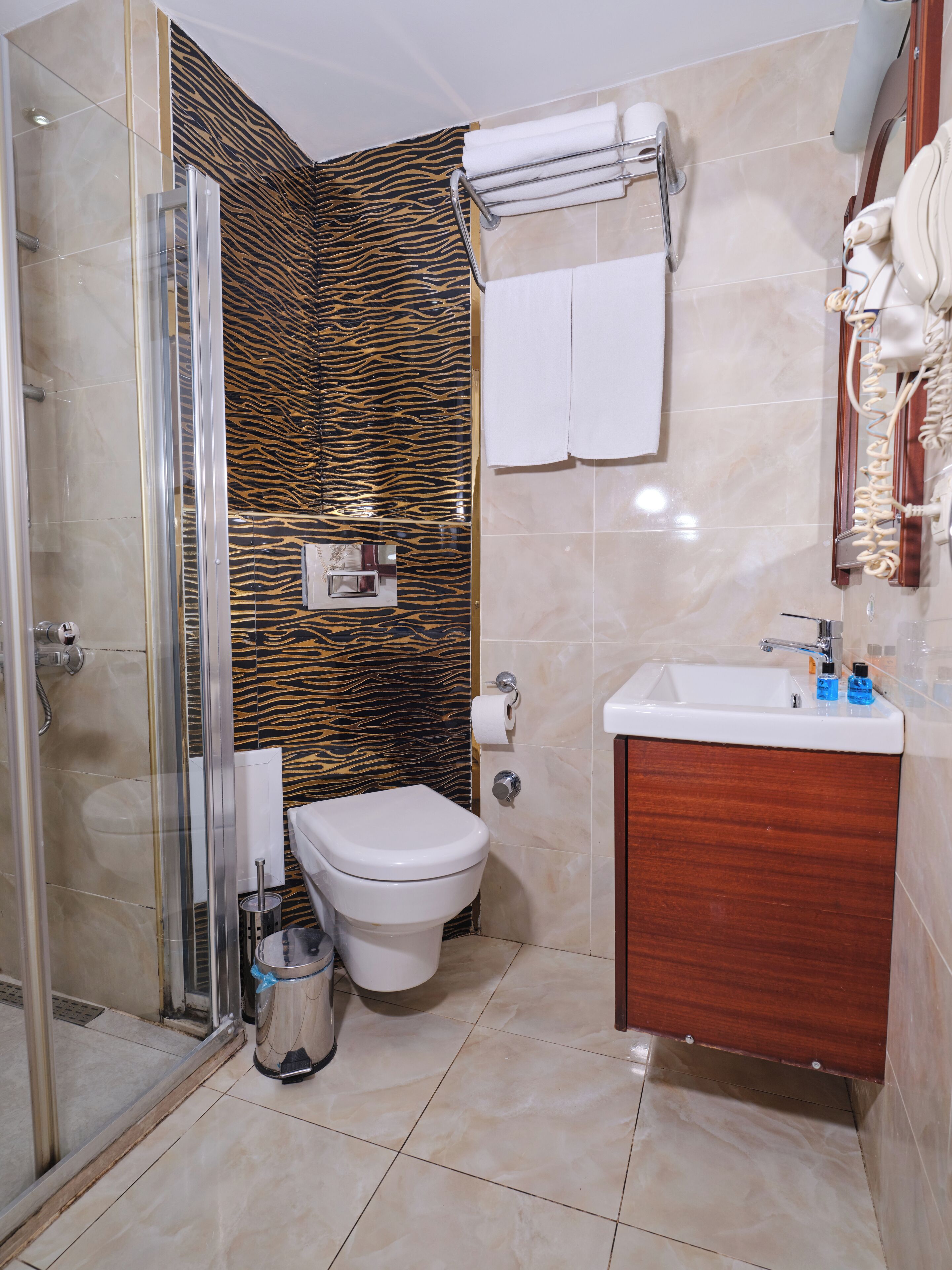 Un baño con cabina de ducha de vidrio, inodoro, lavamanos y toallero.