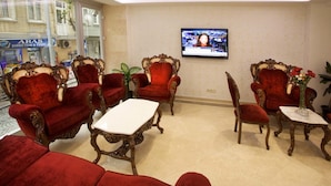 A lobby with red upholstered chairs, a white coffee table, and a television mounted on the wall. - New City Hotel (Istanbul)