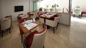 A dining area with multiple tables and chairs, a television mounted on the wall, and large windows with plants. - New City Hotel (Istanbul)
