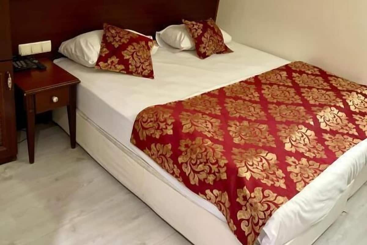 A hotel room with a large bed, two bedside lamps, and a wooden nightstand with a remote control.