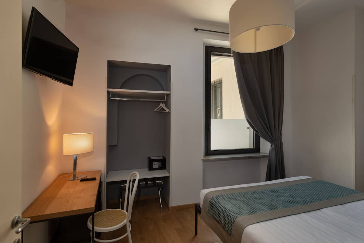 A hotel room with a bed, desk, chair, TV, and a window with curtains.
