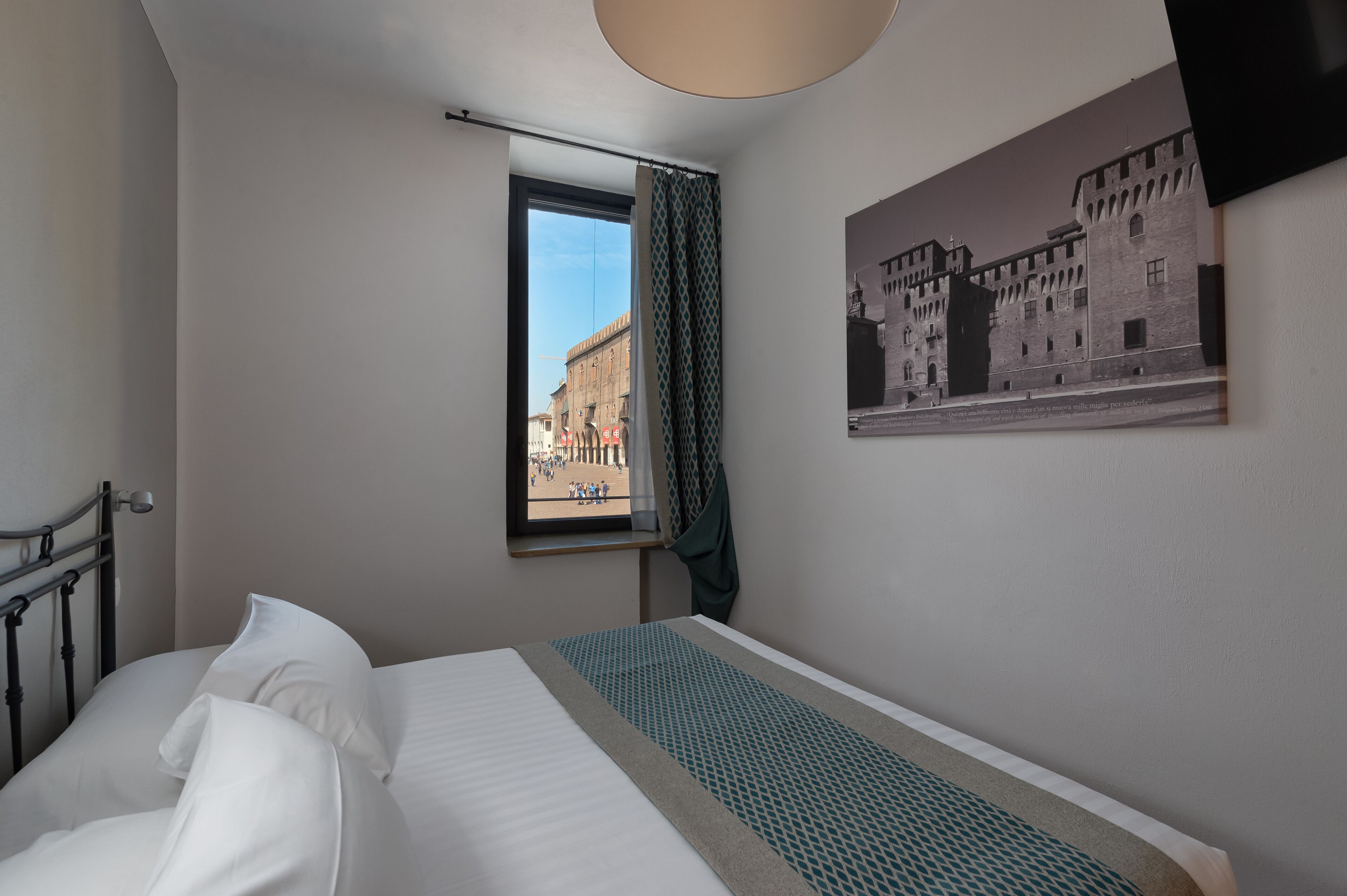 A hotel room with a bed, a window with curtains, and a wall-mounted picture of a building.