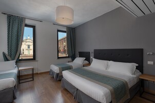 Habitación de hotel con dos camas, una ventana que ofrece vista a un edificio, una lámpara colgante y piso de madera.