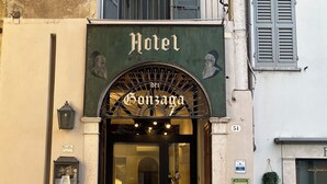 L’entrée de l’hôtel Dei Gonzaga se distingue par son portail classique en arc de cercle, une enseigne indiquant le nom de l’hôtel et un petit espace extérieur aménagé en coin salon, visible depuis l’entrée.