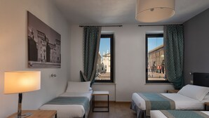 Une chambre d’hôtel avec deux lits, un bureau, une lampe et une fenêtre donnant sur des immeubles.