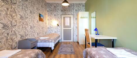 A room with two beds, a desk, a chair, a mirror, a door, and a light fixture.