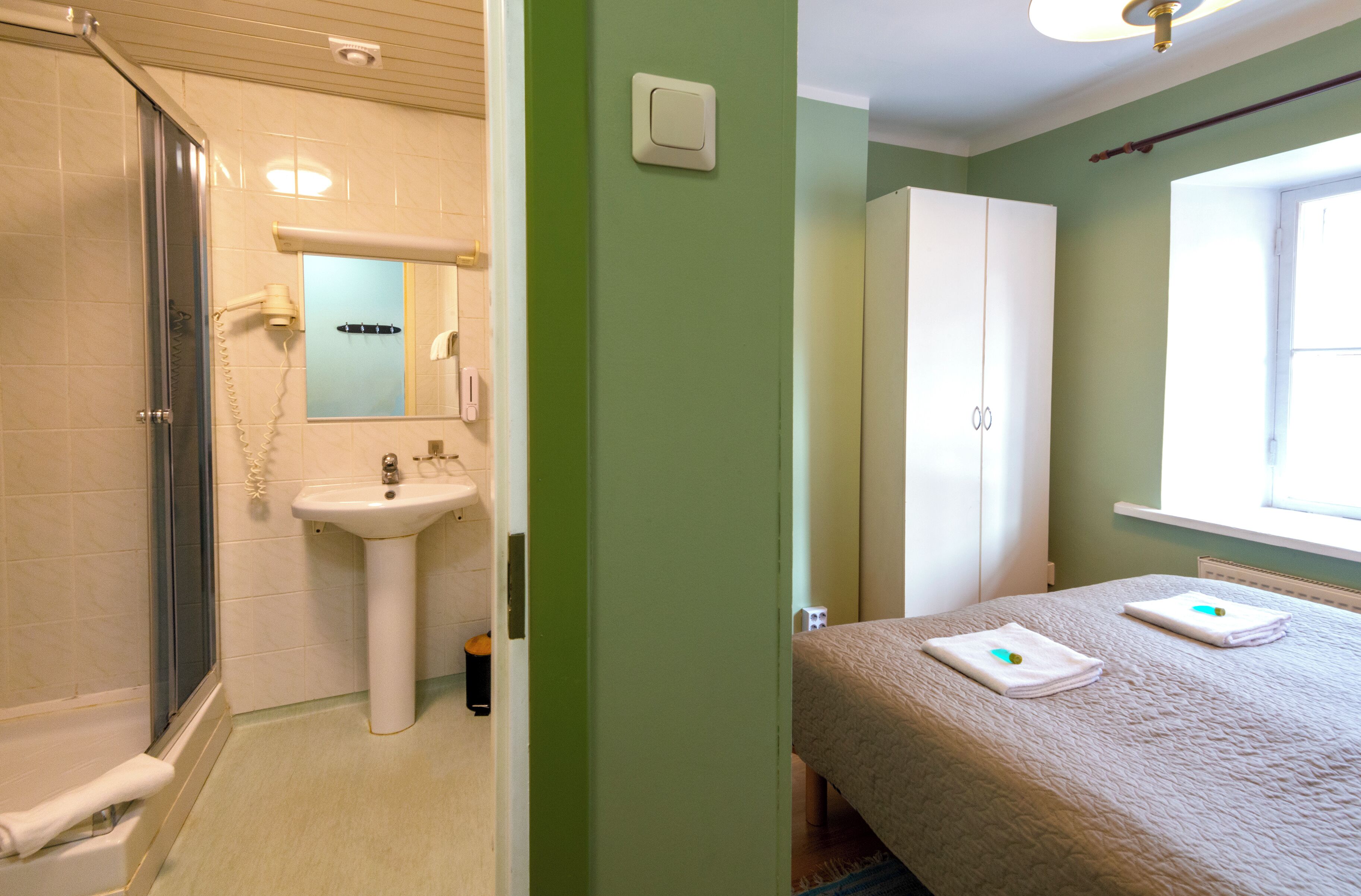A bathroom with a shower, sink, and mirror. There is a bed with towels and a window with a view.