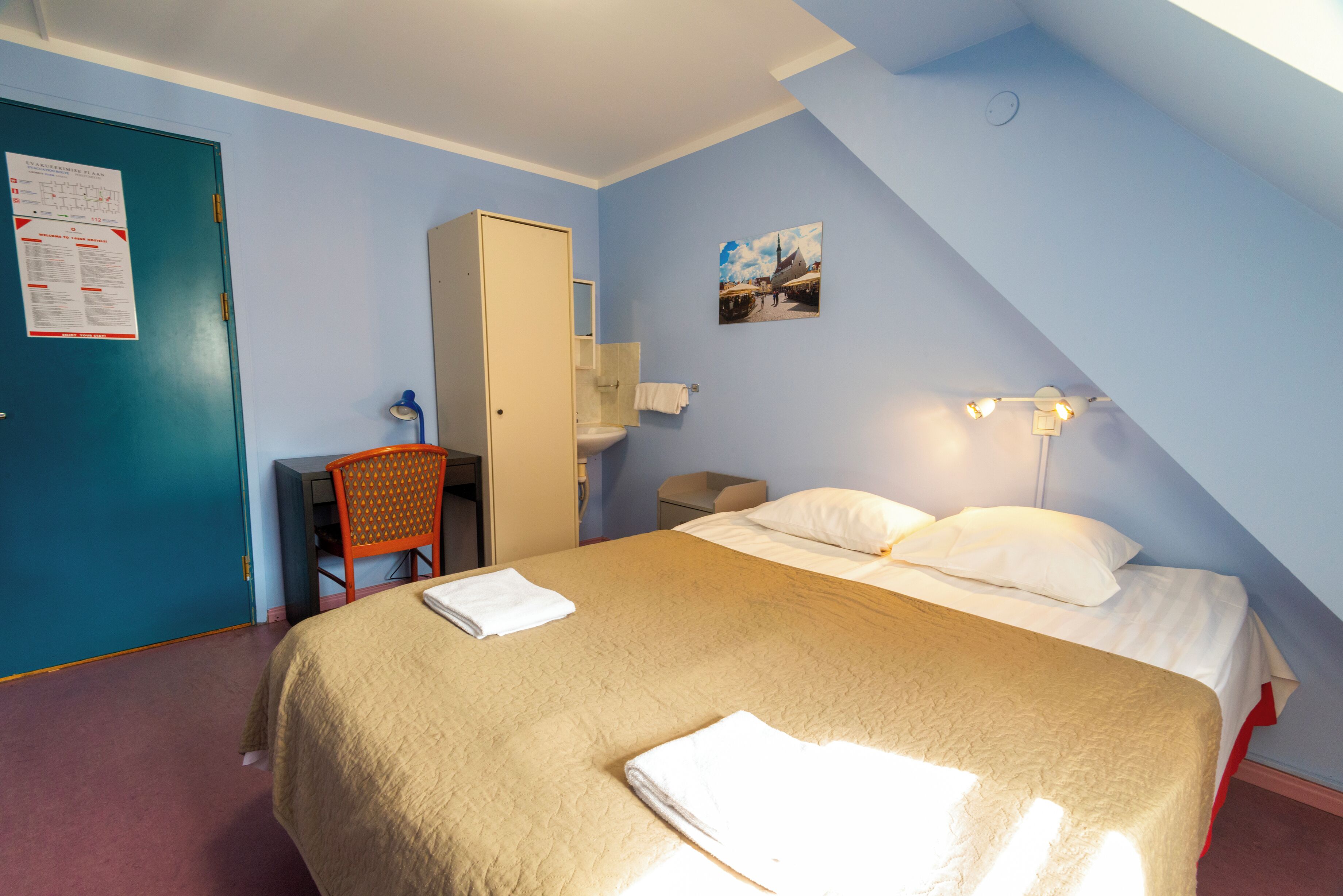 A room with a bed, a desk, a chair, a wardrobe, a bathroom, and a picture on the wall.