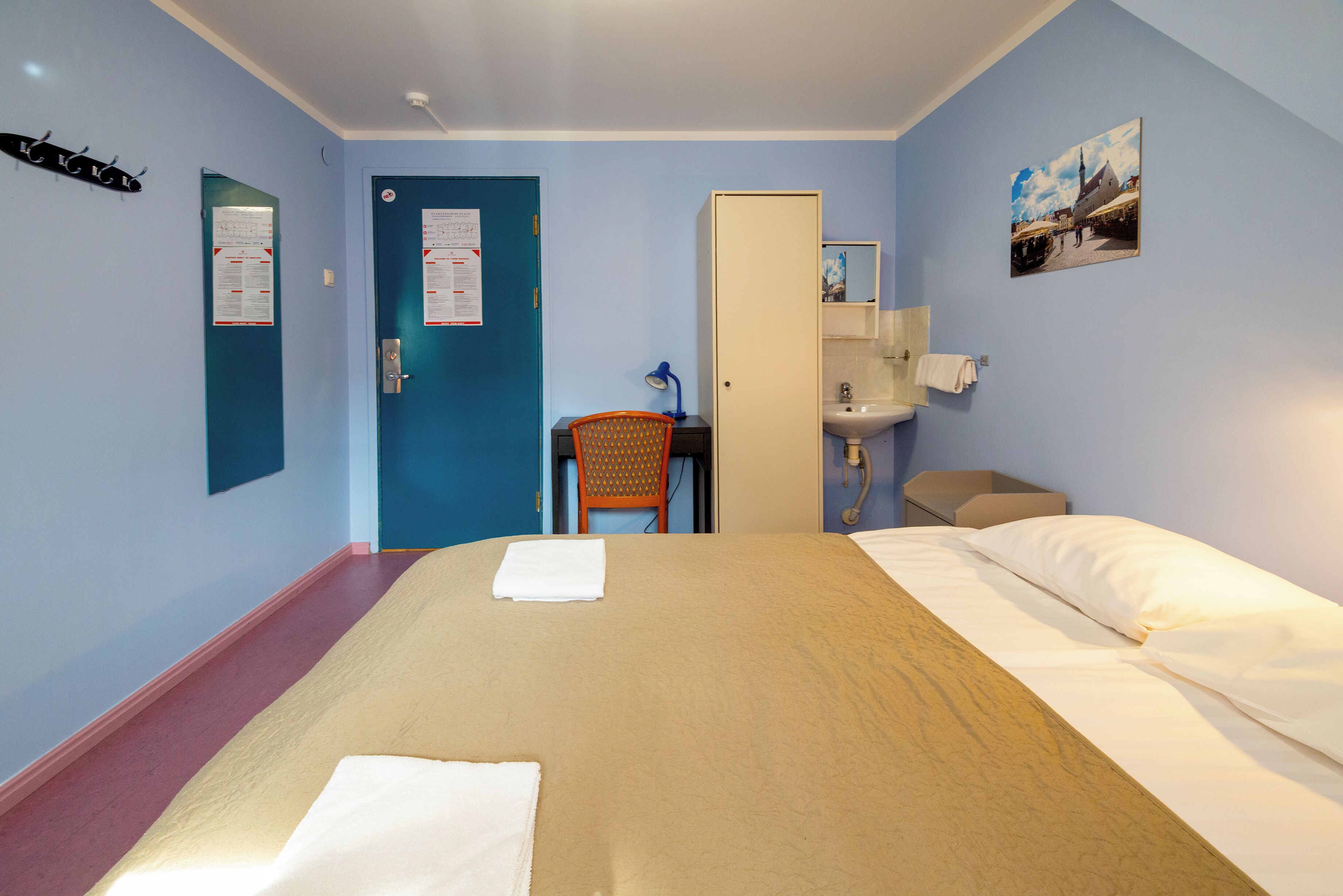 Une chambre d’hôtel avec un lit, un bureau, une chaise, un lavabo et une porte.