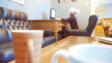 A person using a laptop at a wooden desk in a room with a leather couch and a patterned armchair.