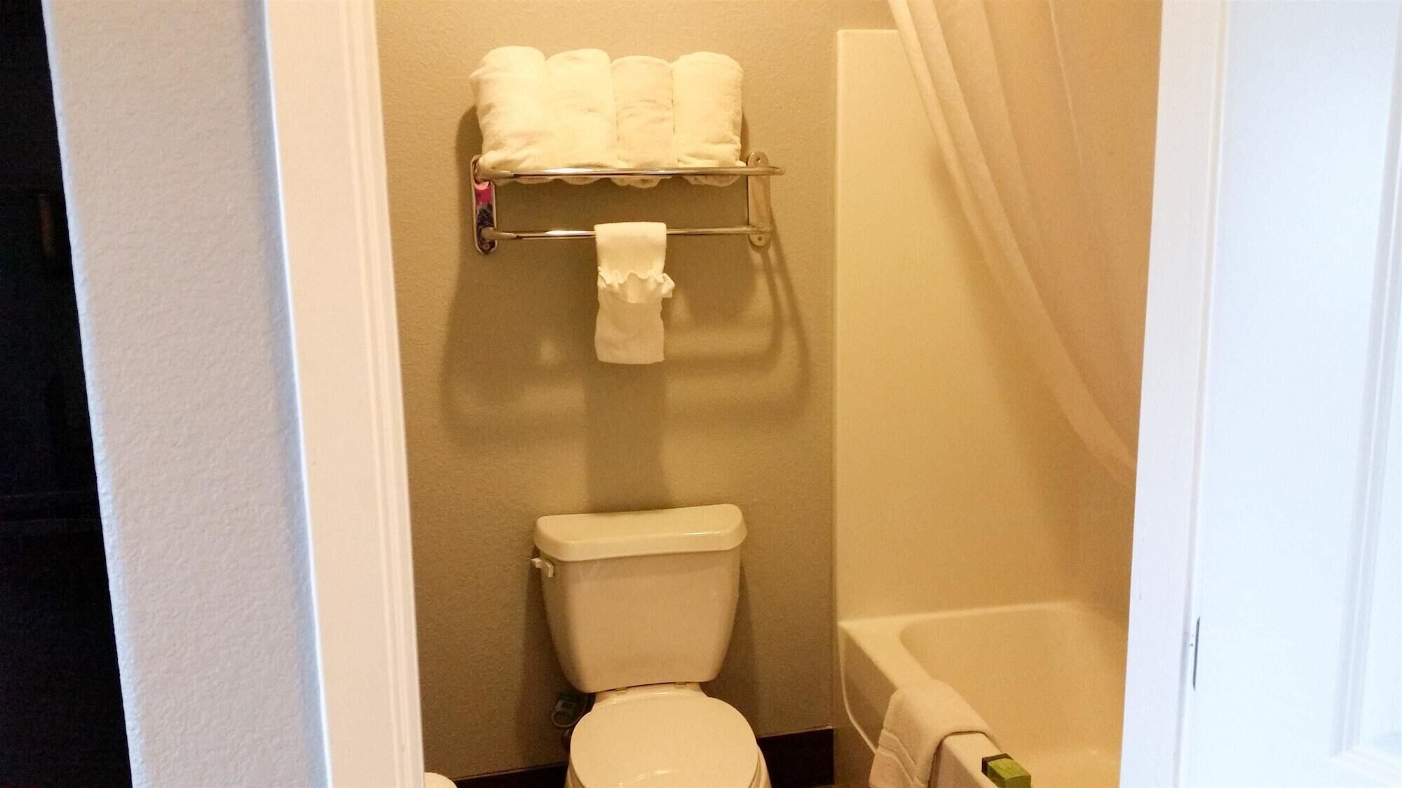 A small bathroom with a toilet, a shelf with towels, and a bathtub.