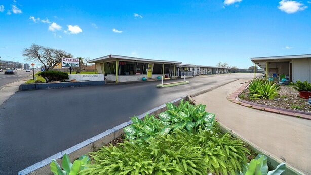 A motel with a welcoming sign, a drive-through service area, and a landscaped garden.