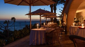 Un espace extérieur aménagé pour les repas, avec des tables et des parasols, offrant une vue sur l’océan.
