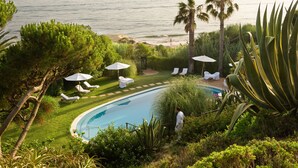 Un espace piscine agrémenté de chaises longues et de parasols, entouré de verdure et offrant une vue sur l’océan.
