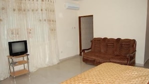 A room with a bed, a television on a stand, a brown woven chair, and a mirror on the wall.