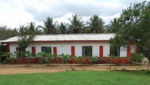 A single-story building with a flat roof, surrounded by greenery and palm trees.
