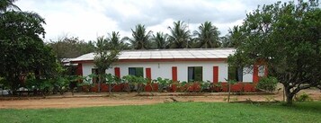 Um edifício térreo com teto plano, rodeado por vegetação e palmeiras.