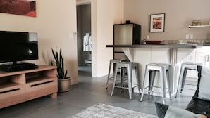 Un salon moderne avec un téléviseur à écran plat, un meuble de rangement en bois, une plante en pot et un tapis gris.