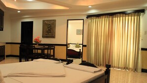 Une chambre d’hôtel avec un lit bien fait, un bureau avec une chaise, une table à manger avec des chaises et une grande fenêtre avec des rideaux.