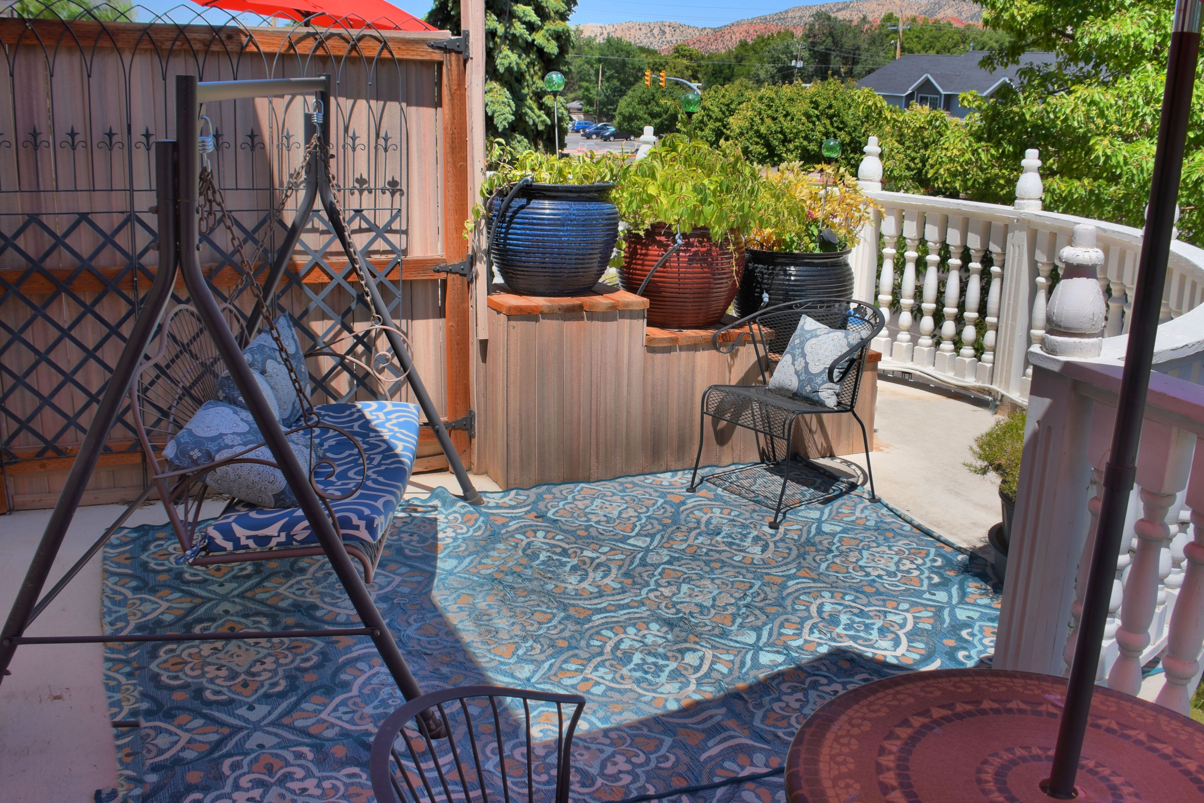 A patio with a swing set, a table with chairs, and potted plants.