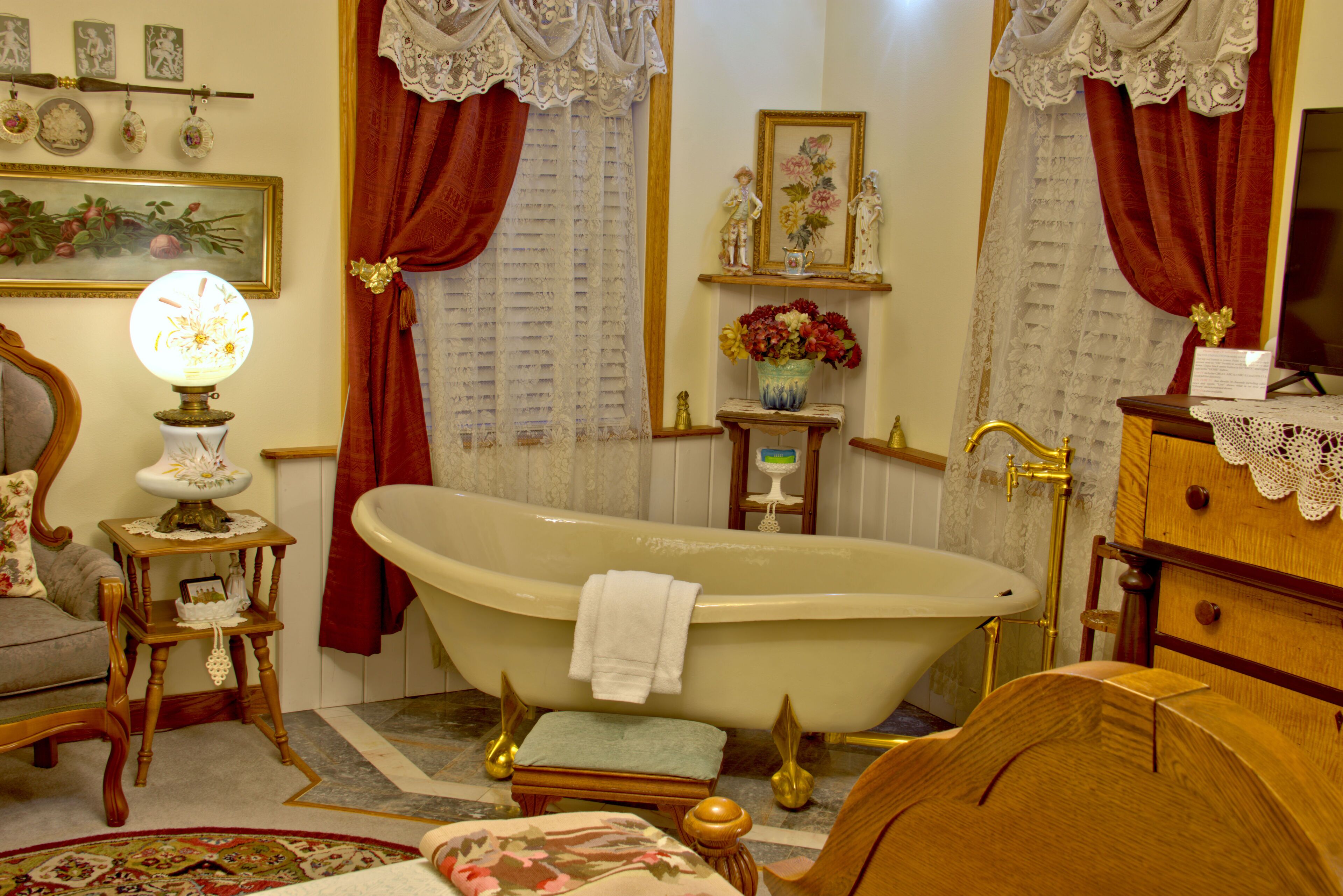 A vintage bathroom with a clawfoot bathtub, a wooden vanity, a small table with a lamp, and a floral rug.