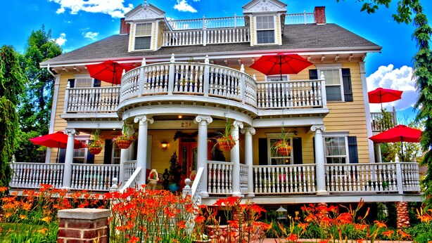 A two-story house with a balcony, red umbrellas, and a flower garden. - Big Yellow Inn (Cedar City)