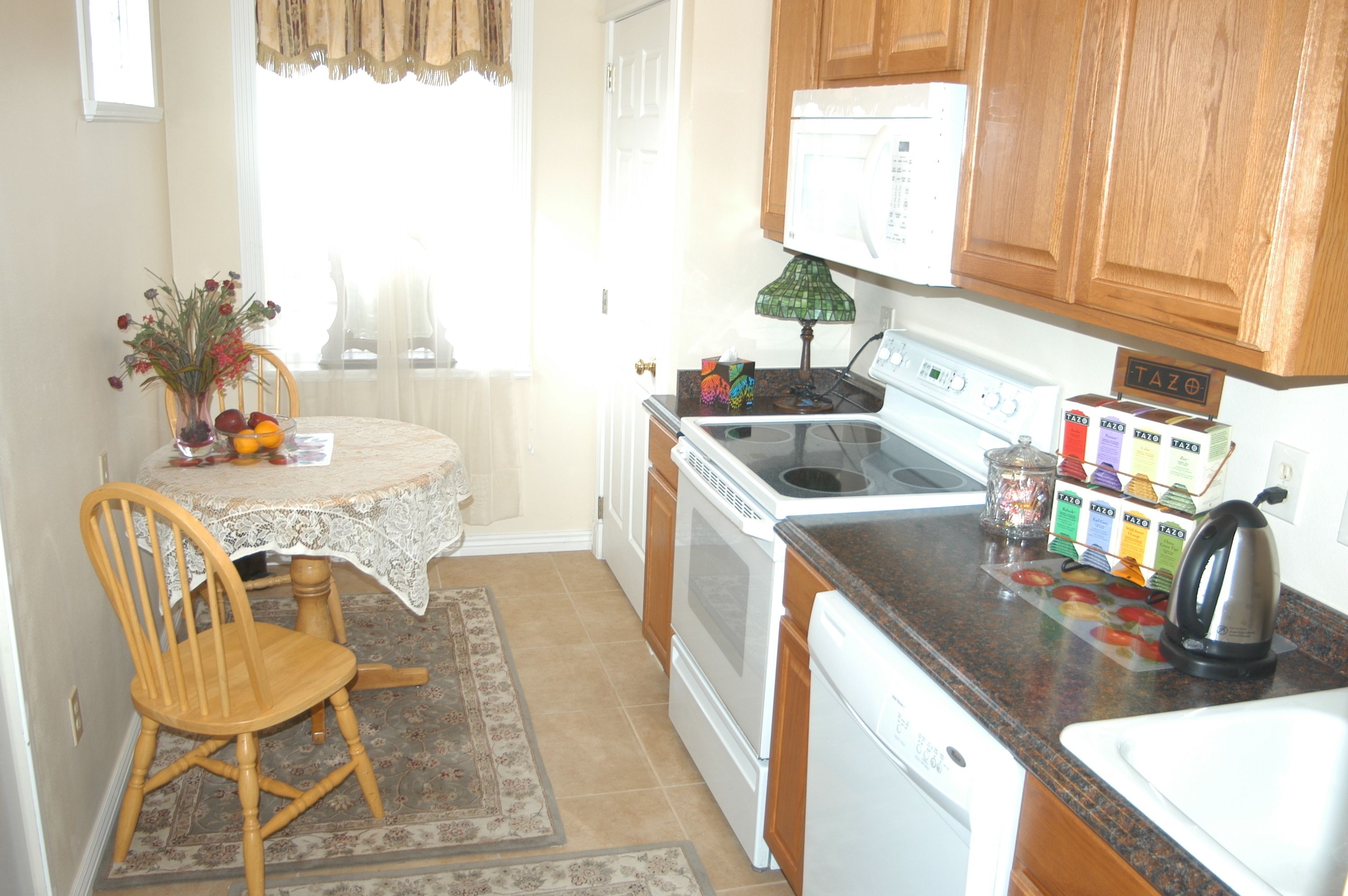 A kitchen with wooden cabinets, a stove, a dishwasher, and a table with a chair.