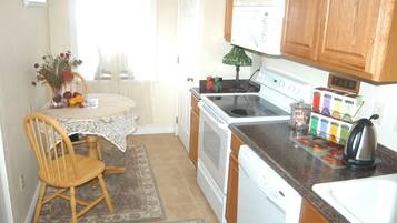 A kitchen with wooden cabinets, a stove, a dishwasher, and a table with a chair.