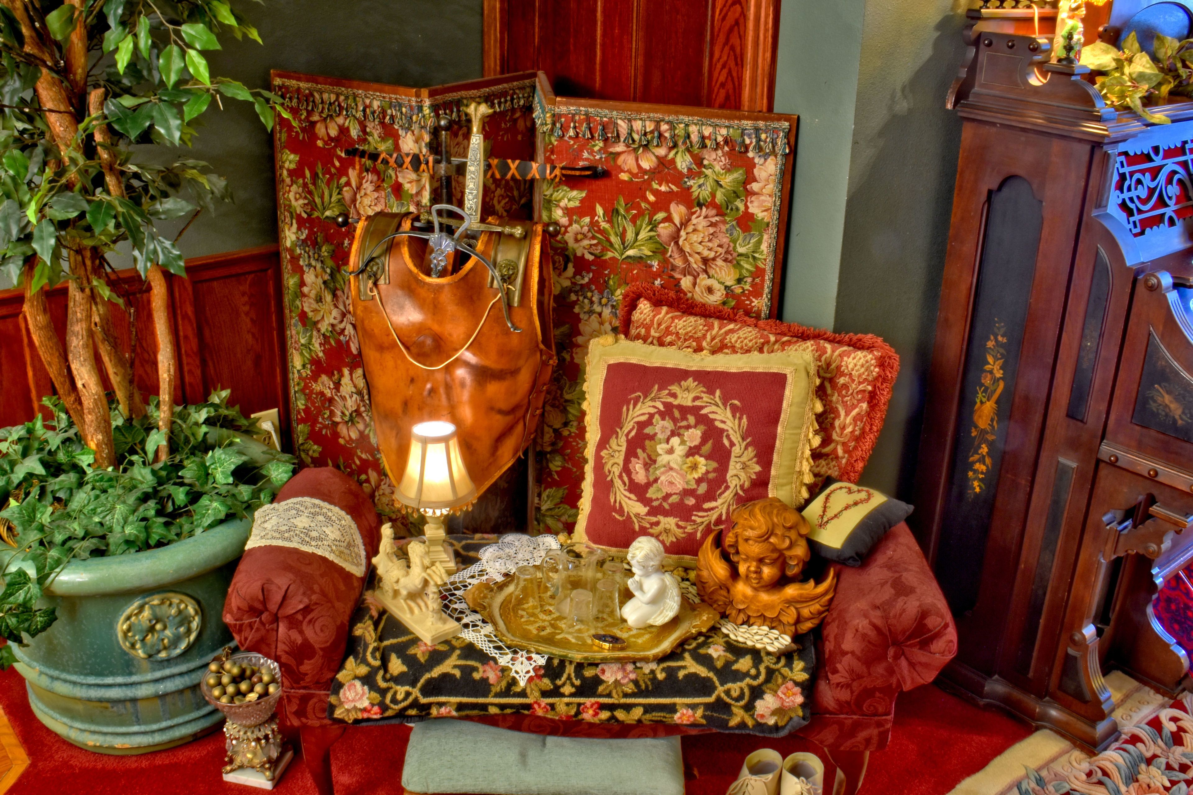 Une pièce comprenant une lampe ancienne, une commode décorative, un canapé rouge moelleux et un meuble en bois.