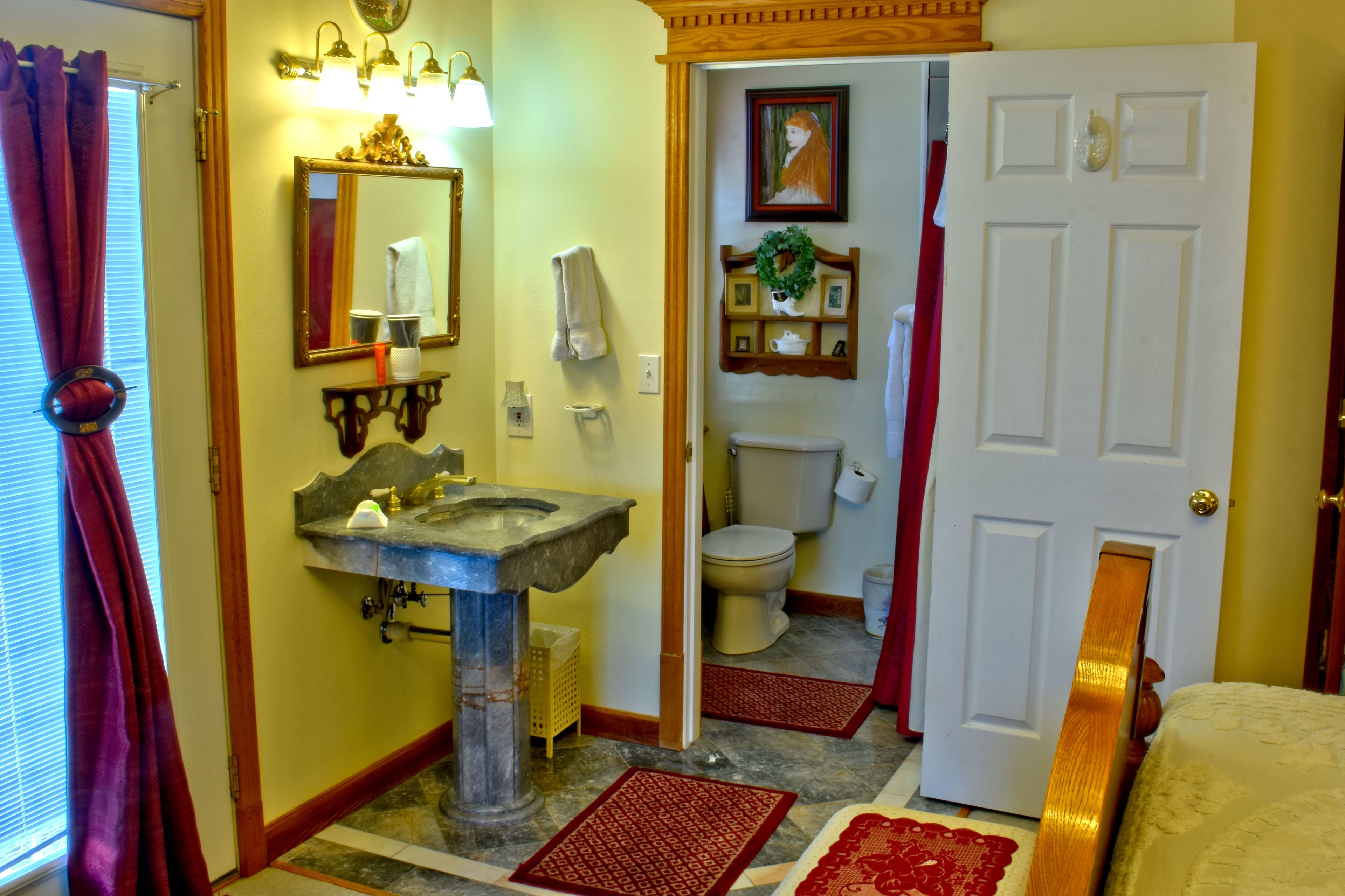 A bathroom with a stone sink, a mirror, a toilet, and a door leading to another room.