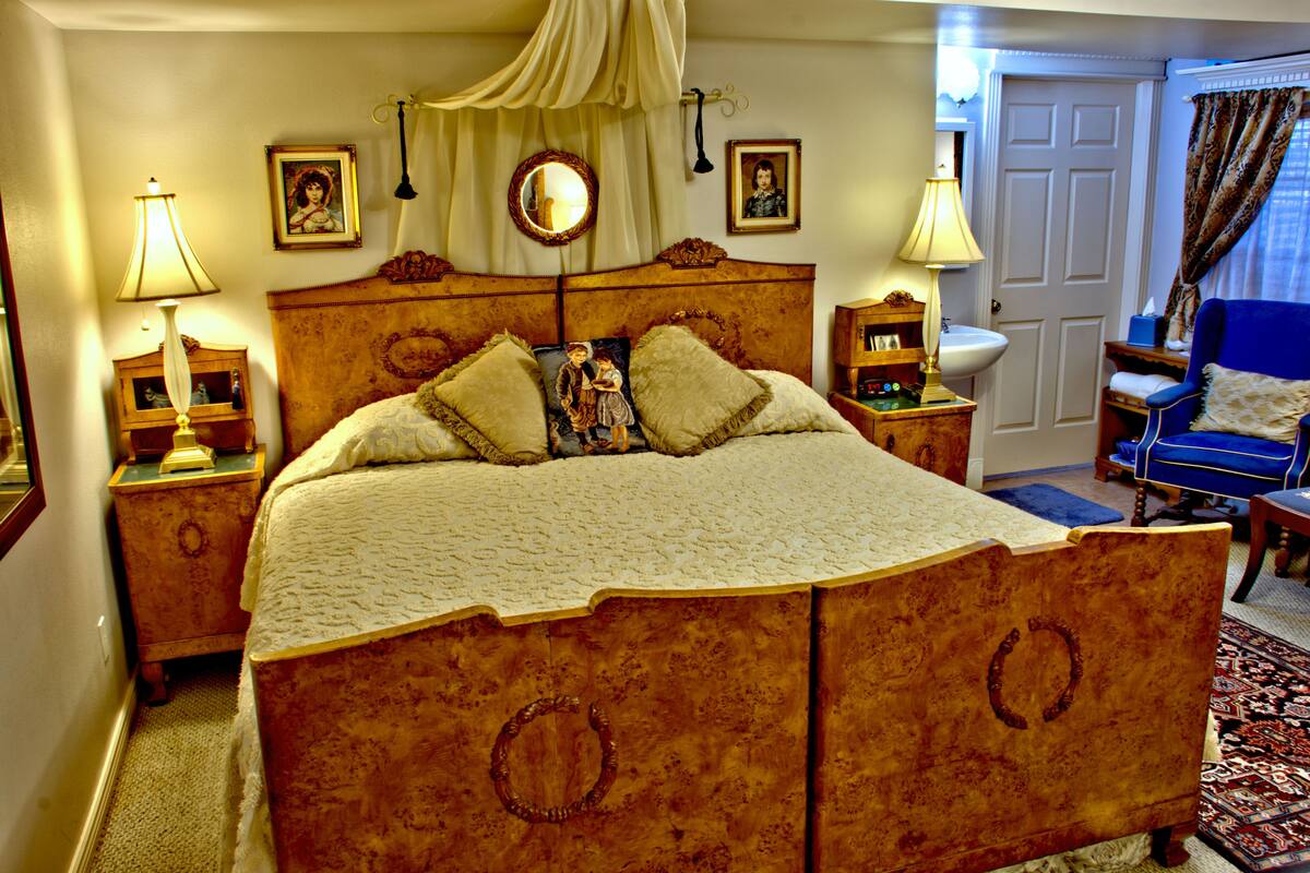 A traditional bedroom with a large bed, bedside tables, a nightstand, a chair, a mirror, and a door.