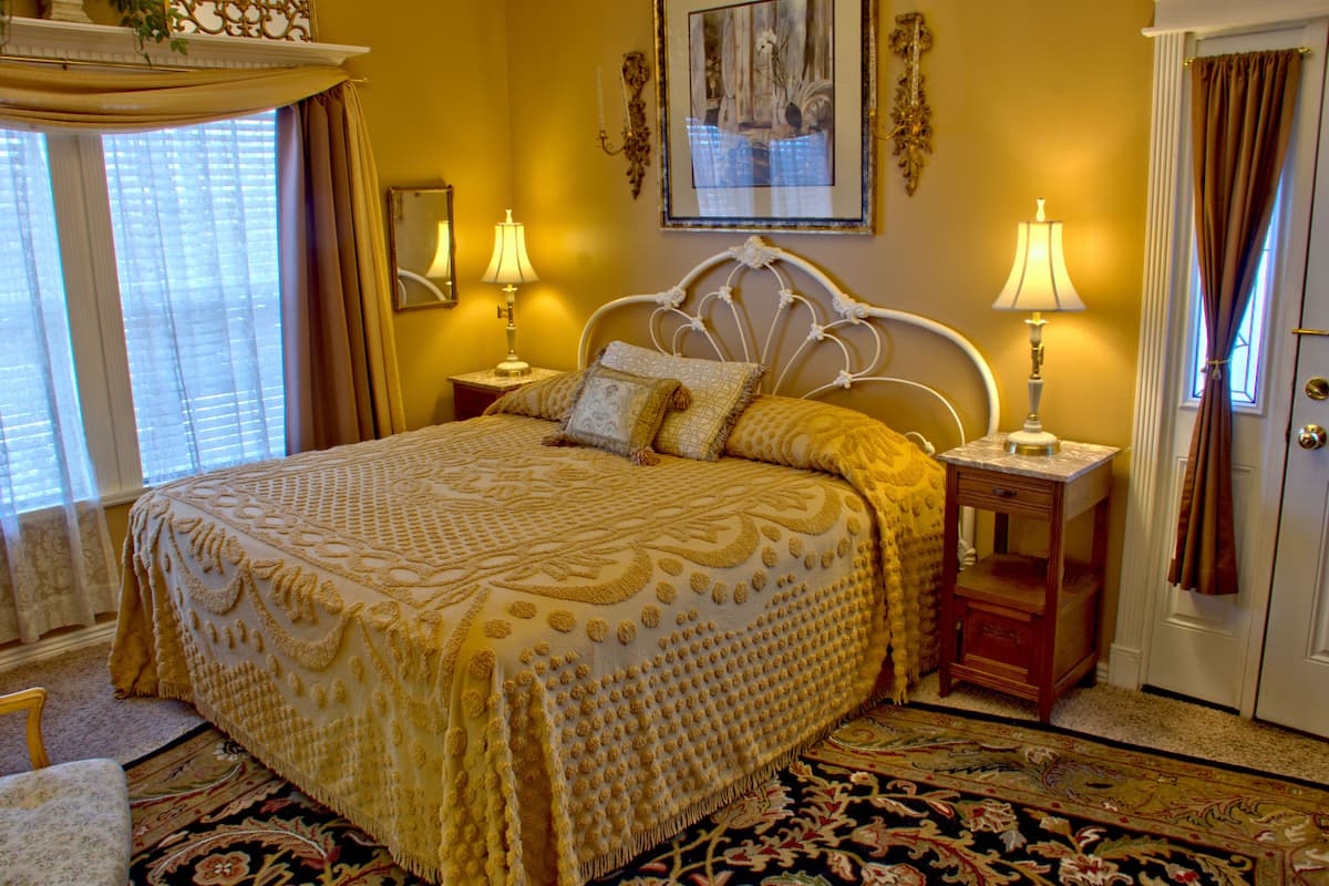 A bed with a patterned bedspread, two bedside lamps, a nightstand, and a floral carpet.