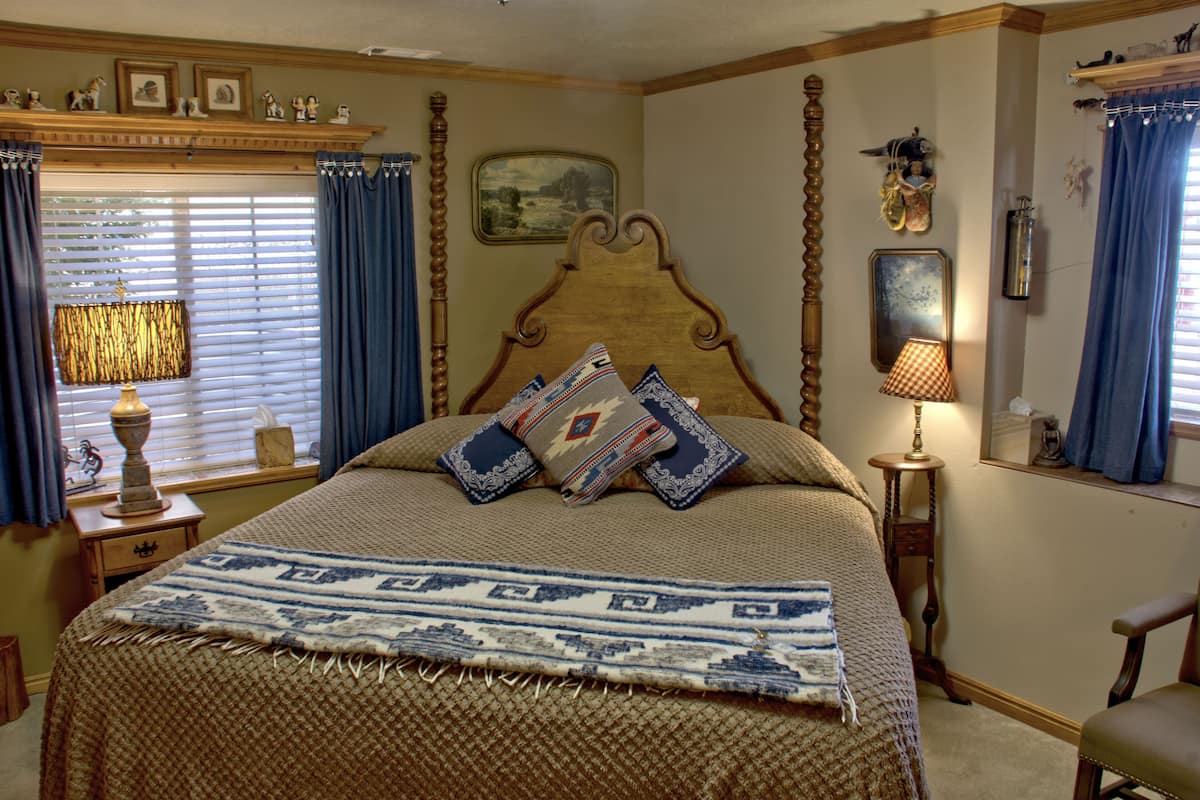 A bedroom with a large bed, a nightstand, a lamp, a chair, and a window with curtains.
