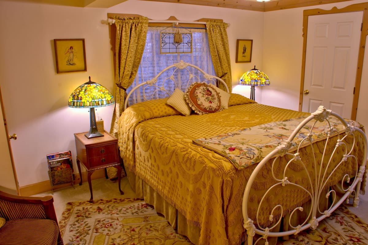 A bedroom with a bed, two bedside tables, a nightstand, a window with curtains, and a door.