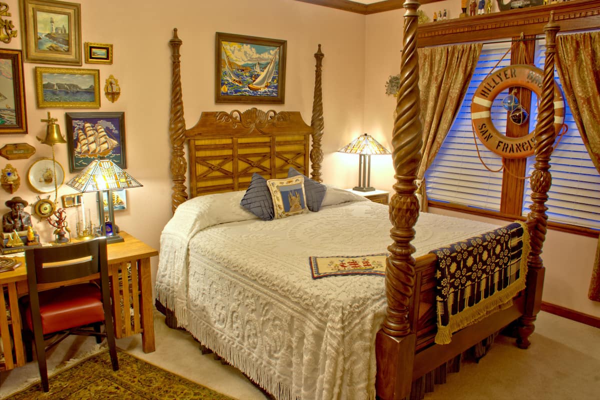 A four-poster bed with a canopy, a wooden desk with a chair, and various decorative items including framed pictures and a life preserver.