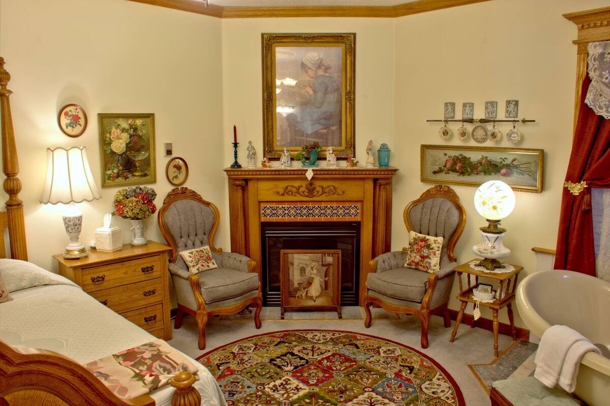 A traditional room with a fireplace, two armchairs, a bed, and a round rug.