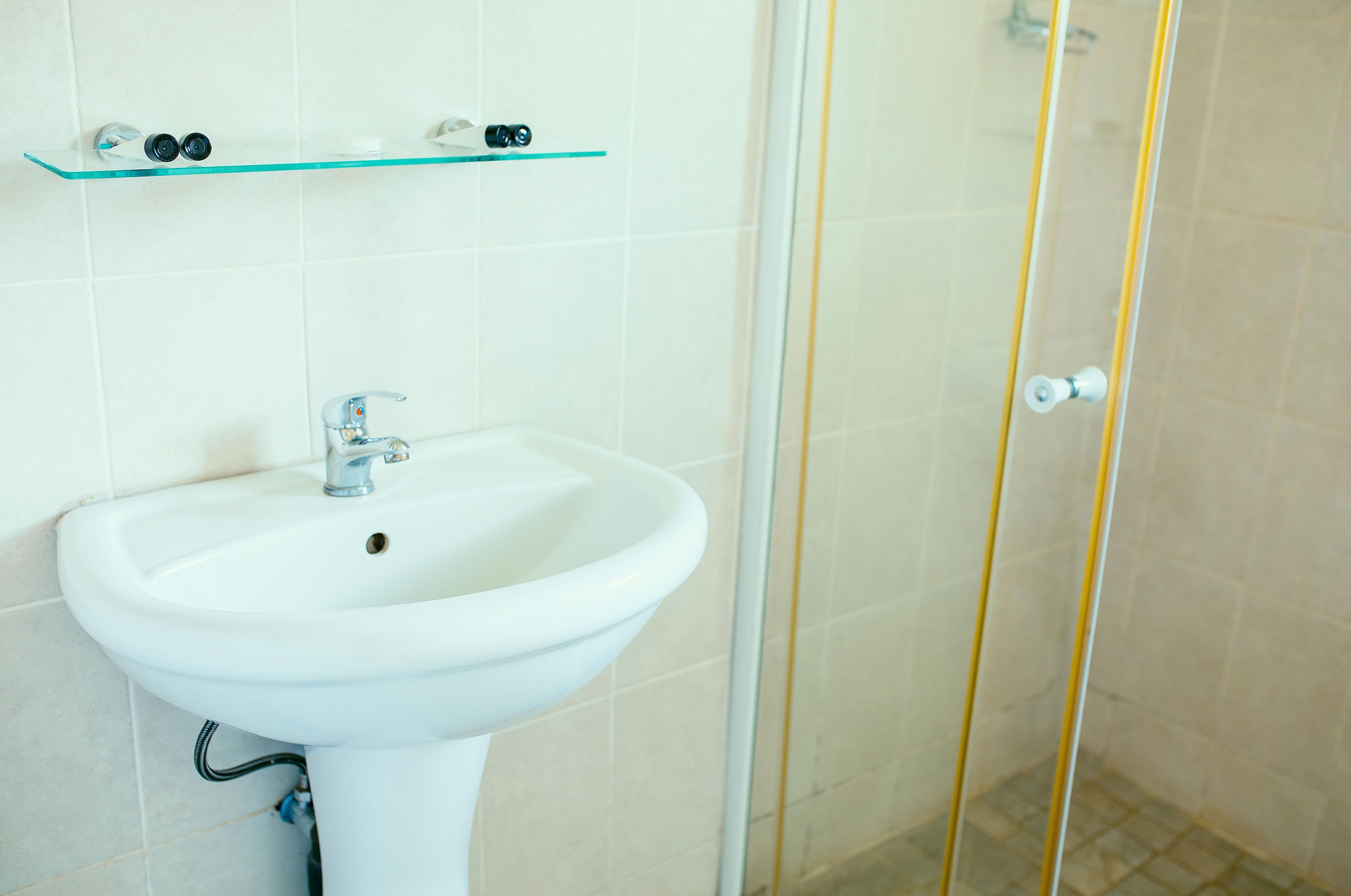 A bathroom with a white sink, a glass shelf above it, and a glass shower enclosure.