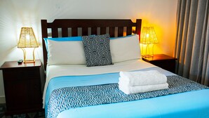 Un lit bien fait, recouvert d’une couvre-lit à motifs bleus et blancs, avec un oreiller blanc et une serviette blanche pliée posée sur le lit. Deux tables de chevet, chacune avec une lampe, se trouvent de chaque côté du lit.