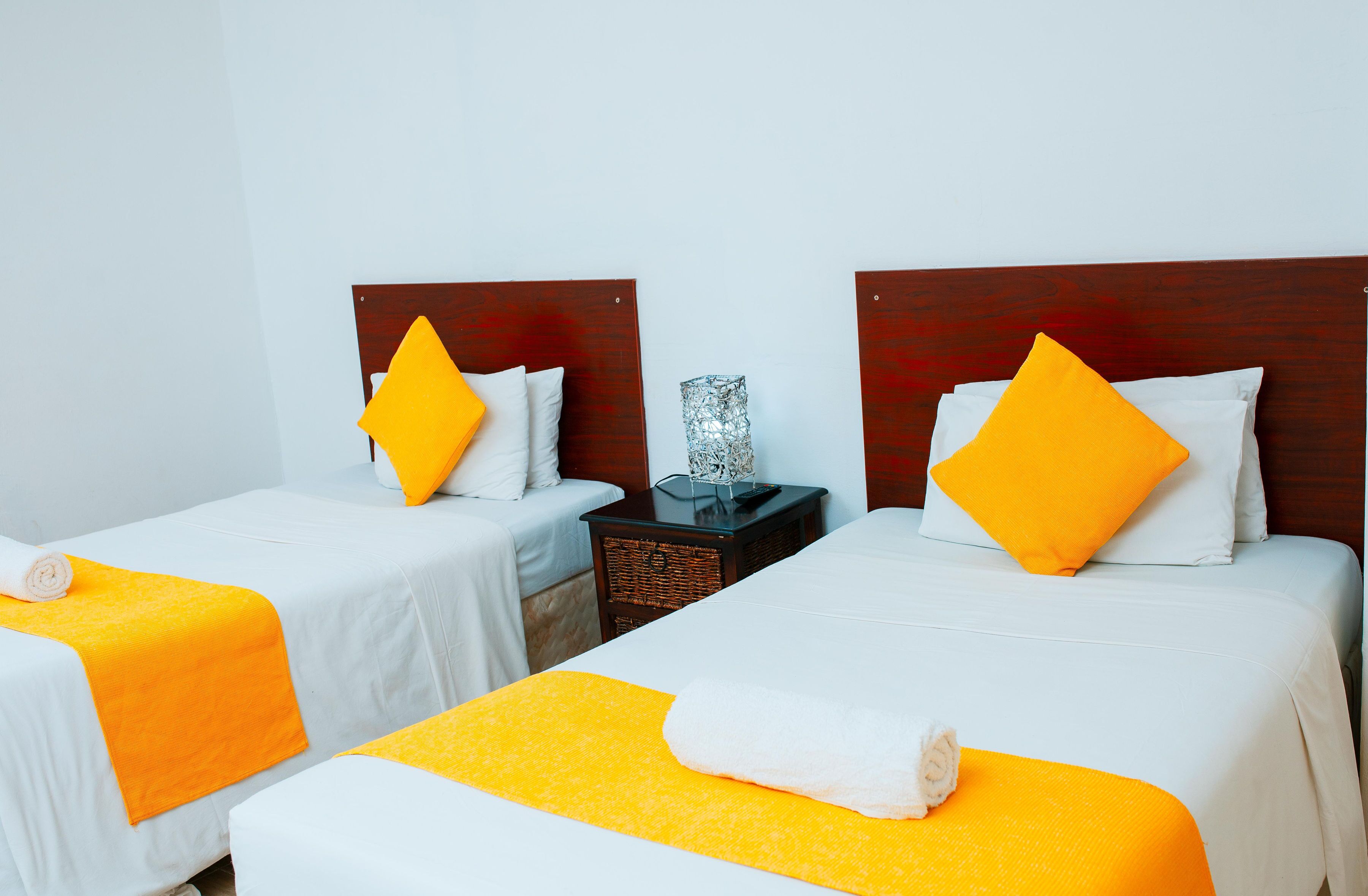 Deux lits simples avec des têtes de lit en bois, du linge de lit blanc et des touches de couleur orange.
