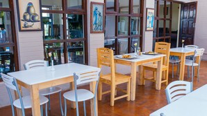 Un espace repas avec des tables et des chaises en bois, de grandes fenêtres et des œuvres d’art accrochées aux murs.