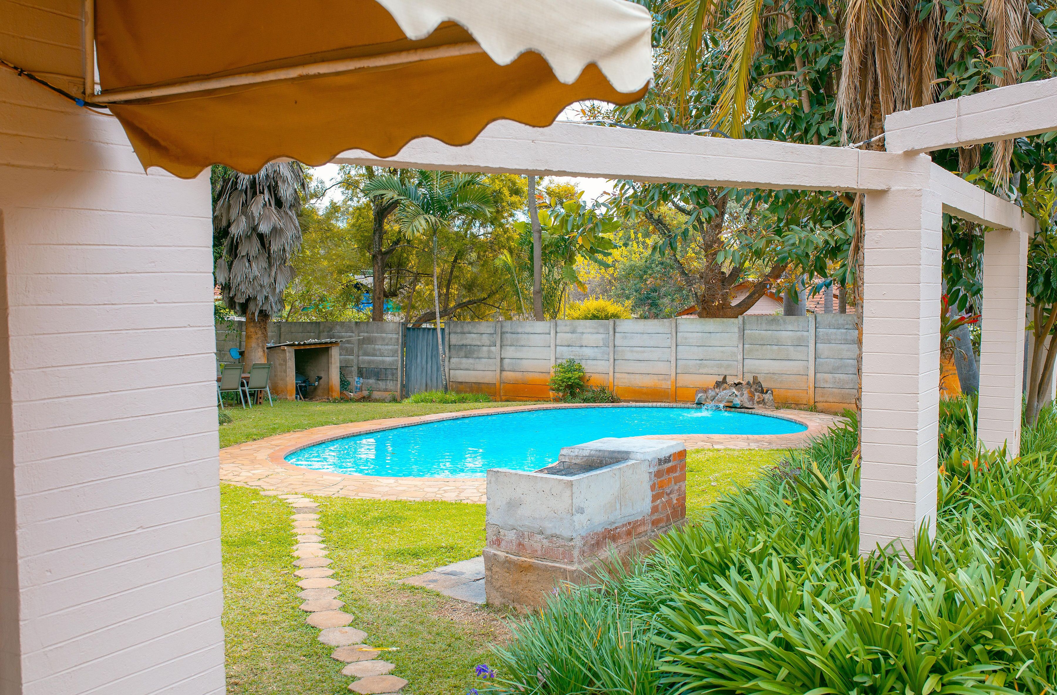 Un patio trasero con piscina, zona de barbacoa y terraza cubierta.